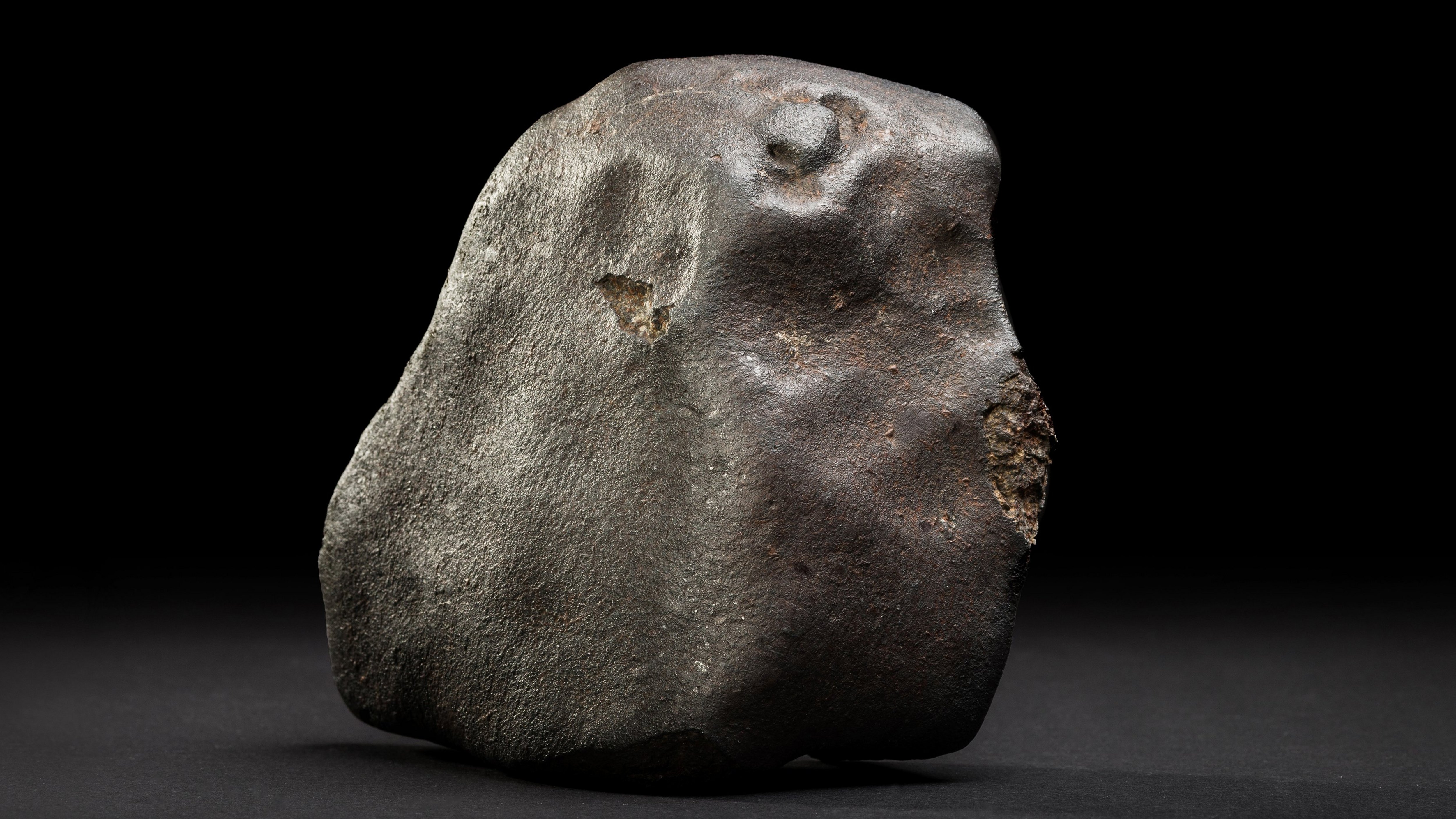 Ein grauer Klumpen Meteorit vor dunklem Hintergrund