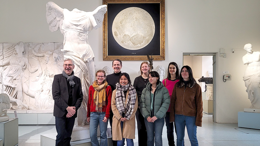 Gruppenfoto der Mitarbeitenden des ICFA unter Thomas Vautravers mit Ernst Seidl im Rittersaal; im Hintergrund die Nike von Samothrake und das Mondgemälde mit realistisch modellierten Kratern