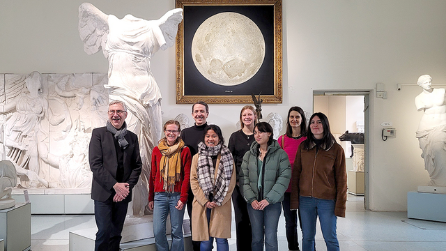 Gruppenfoto der Mitarbeitenden des ICFA unter Thomas Vautravers mit Ernst Seidl im Rittersaal; im Hintergrund die Nike von Samothrake und das Mondgemälde mit realistisch modellierten Kratern