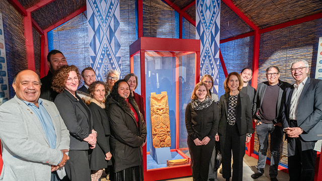 Prominente Persönlichkeiten der Koorperation zwischen Te Aitanga-a-Hauiti, des Wissenschaftsministeriums Baden-Württemberg und der Universität Tübingen sowie dem Museum der Universität Tübingen MUT vor der beleuchteten Vitrine von Hinematioros Pou (mittig)