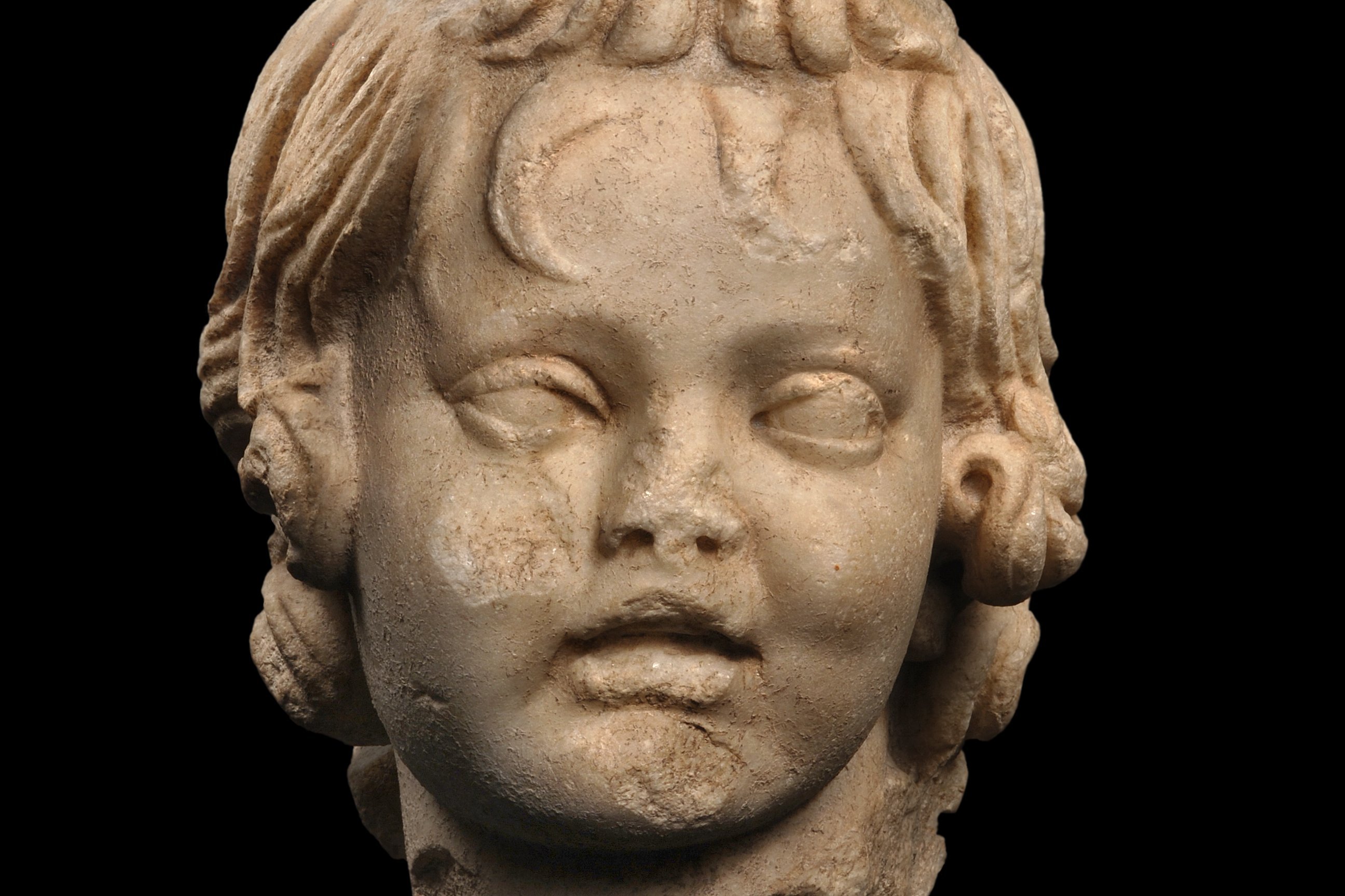 Marble head of a boy with his hair falling into his forehead, looking at the viewer