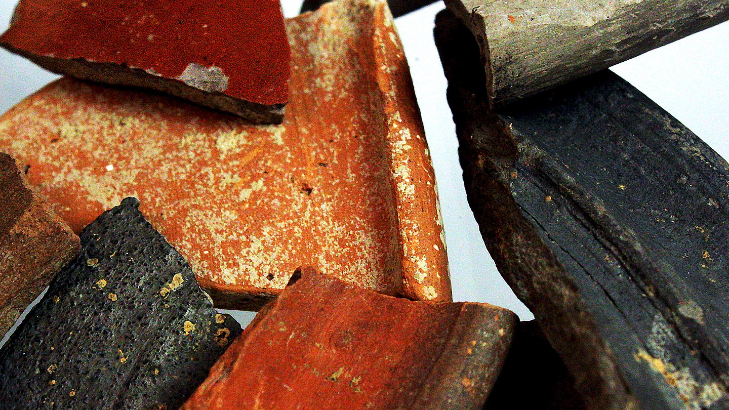 Foto: MUT Ausschnitt eines Blicks auf verschiedene schwarze, rote und rotbraune Tonscherben vor beleuchtetem Hintergrund