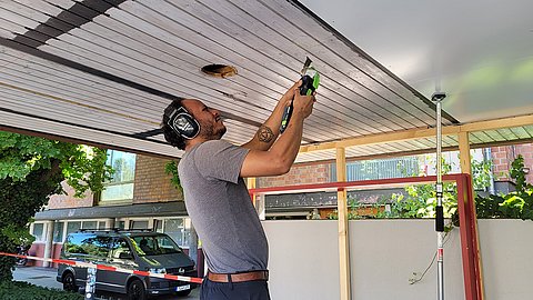 Leonardo Sarmiento mit Gehörschutz bohrt an den Deckenpanelen im Außenbereich