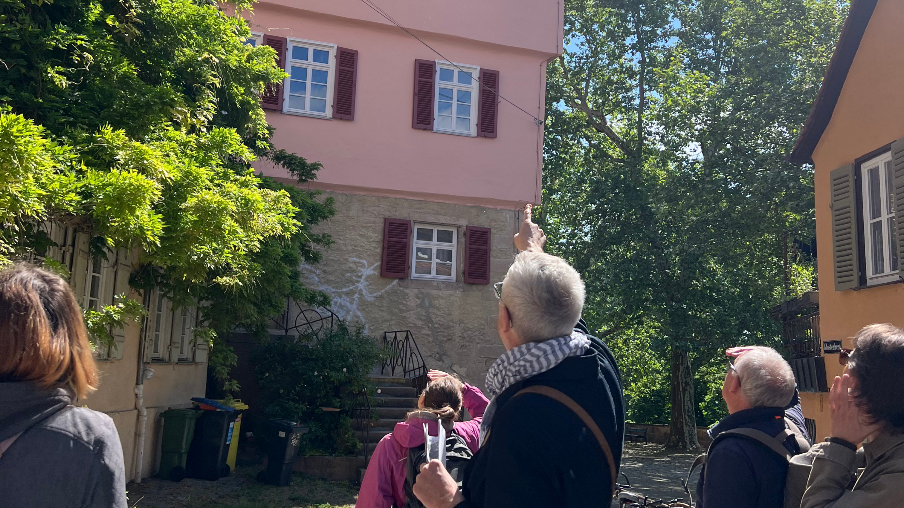 Im Vordergrund stehen Seminarteilnehmende mit dem Rücken zur Kamera und folgen mit dem Blick dem Fingerzeig des in der Mitte stehenden Prof. Seidl, der auf ein Haus in der Tübinger Altstadt mit rosa Fassade verweist