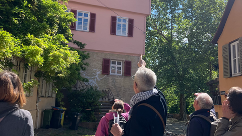 Foto: MUT | Diellëza Hyseni Im Vordergrund stehen Seminarteilnehmende mit dem Rücken zur Kamera und folgen mit dem Blick dem Fingerzeig des in der Mitte stehenden Prof. Seidl, der auf ein Haus in der Tübinger Altstadt mit rosa Fassade verweist