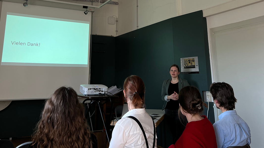 Leinwand mit Projektion einer Folie "Vielen Dank", rechts Dr. des. Annika Vosseler im Vortrag und im Vordergrund zuhörendes Publikum