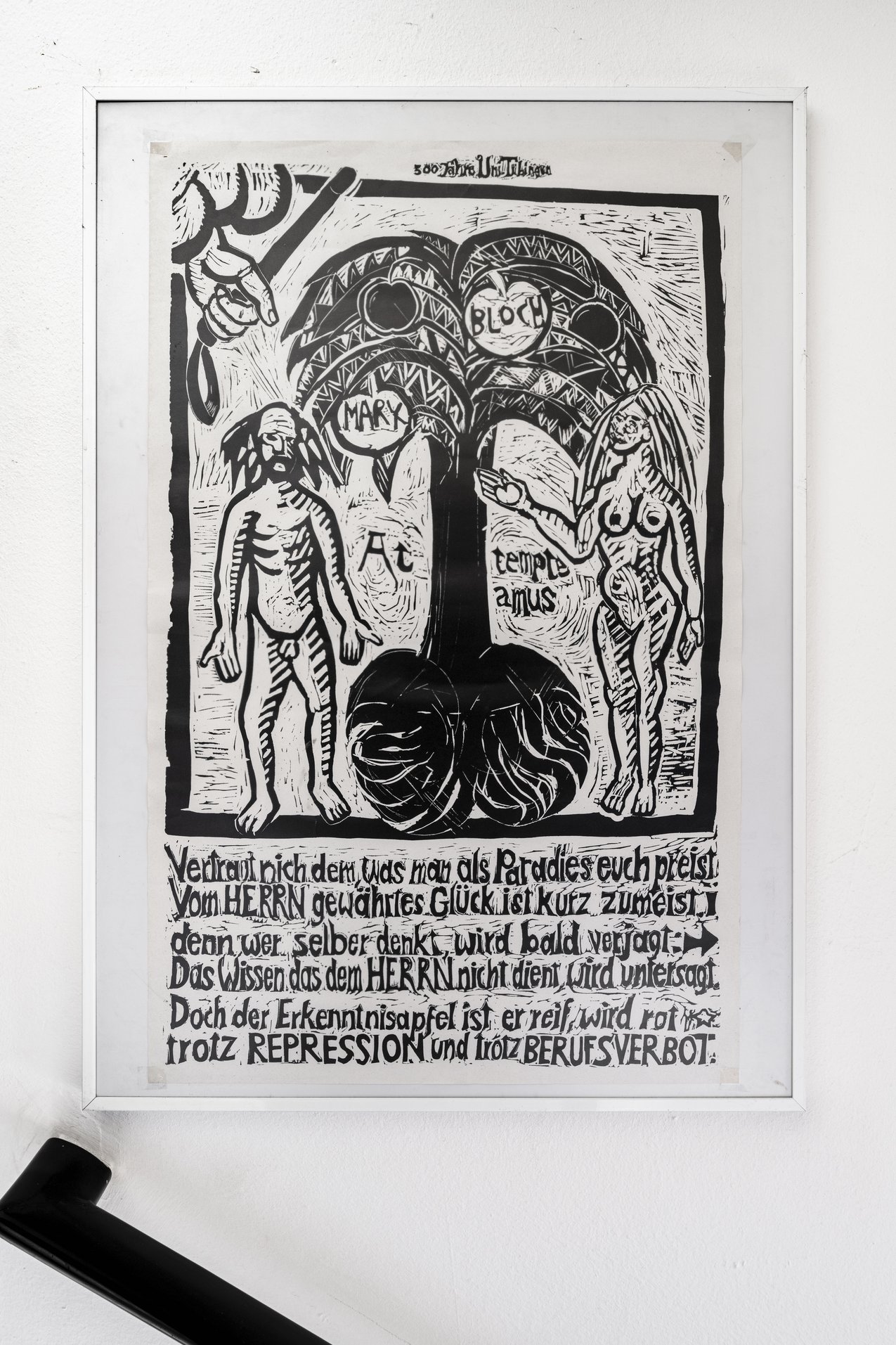 Schwarz-weißes Linoldruck-Poster in einem weißen Rahmen. Das Motiv zeigt zwei nackte, stilisierte menschliche Figuren links und rechts eines Baumes mit großen Blättern und Schriftzügen. Unter dem Bild befindet sich ein mehrzeiliger deutscher Text in handschriftlicher, künstlerischer Schriftgestaltung.