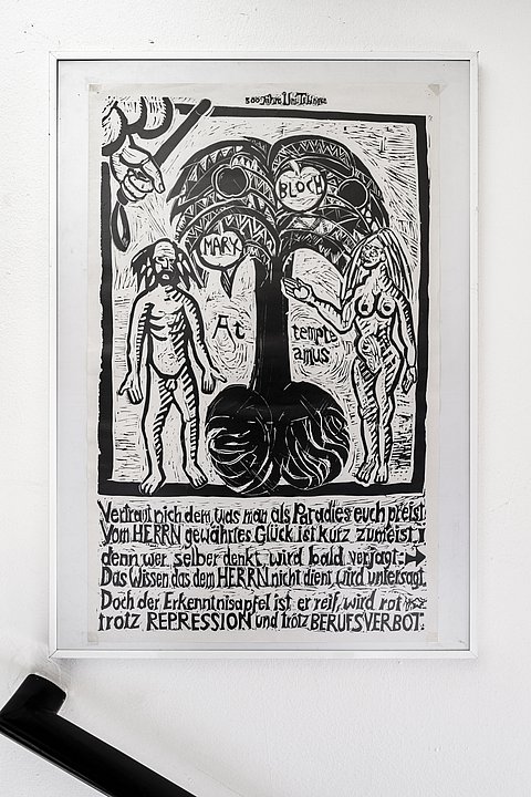 Schwarz-weißes Linoldruck-Poster in einem weißen Rahmen. Das Motiv zeigt zwei nackte, stilisierte menschliche Figuren links und rechts eines Baumes mit großen Blättern und Schriftzügen. Unter dem Bild befindet sich ein mehrzeiliger deutscher Text in handschriftlicher, künstlerischer Schriftgestaltung.