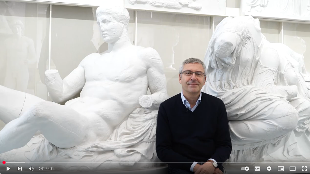 Video frame of Prof Seidl in front of two plaster casts of classical statues in the Museum Ancient Cultures