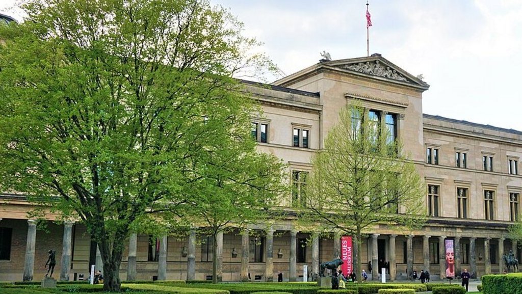 Schräger Blick auf das Neue Museum in Berlin mit palaisartiger Fassade und Arkaden im Erdgeschoss; davor Grasfläche und Begrünung