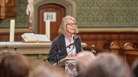SFB-Sprecherin Professorin Dr. Annette Gerok-Reiter spricht ins Mikrophon am Pult, im Vordergrund die unscharfe Rückansicht der Köpfe der Zuhörenden