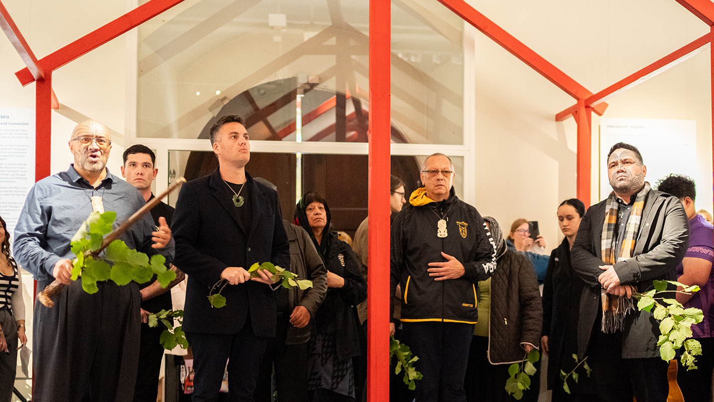 Teilnehmende Maori der Zeremonie am Eingang des stilisierten Versammlungshauses des Ausstellungsaufbaus mit begrünten Zweigen in den Händen