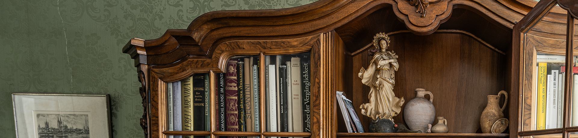 Voller Bücherschrank aus dunklem Holz vor grüner Tapete