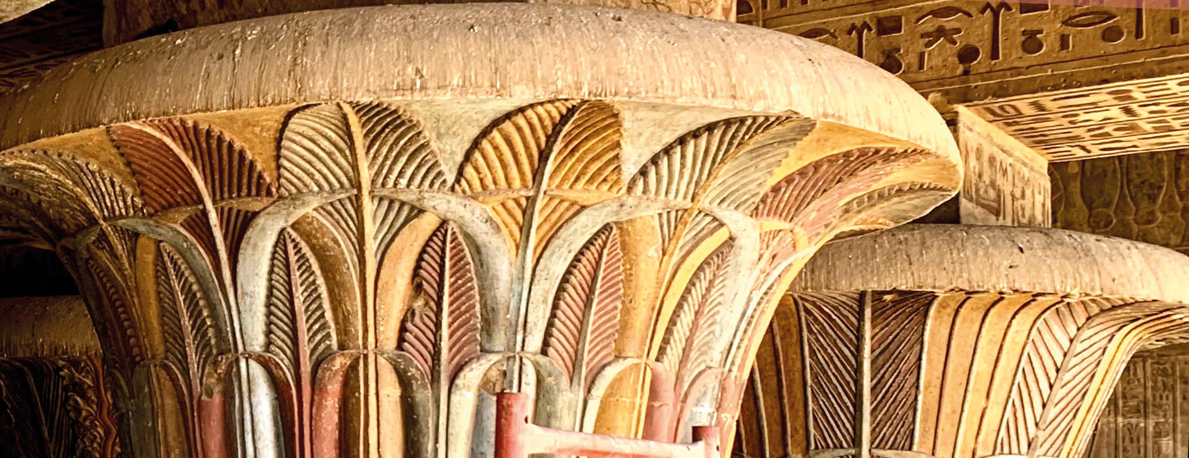 In Beige- und Rottönen gefasste Säulenkapitelle mit Fluchtpunkt rechts im Bild, darüber Deckenbalken mit Hieroglyphen