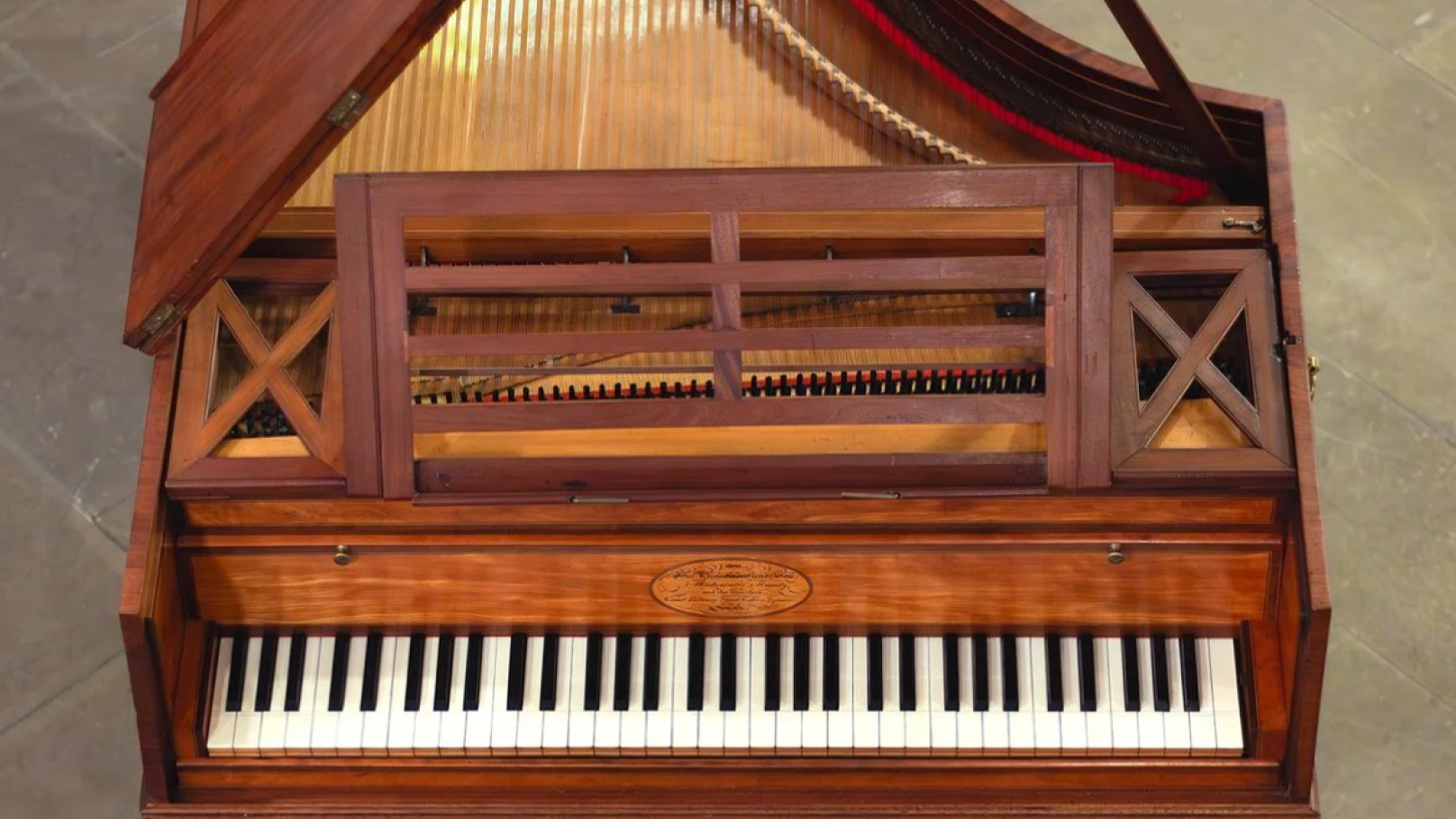 Top view of a historical keyboard instrument made of reddish-brown wood and featuring an empty music stand