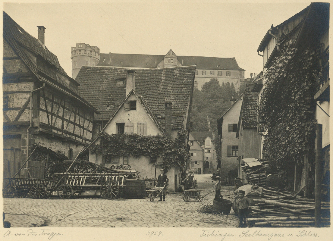 Historische Photographie einer Kreuzung zweier schmaler, gepflasteter Straßen mit Fachwerkhäusern mit steilen Dächern darum herum, im Hintergrund erhebt sich Schloss Hohentübingen; darunter steht handschriftlich notiert "A. von der Trappen, 3959, Tübingen, Seelhausgasse am Schloss"